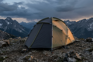 Four-season dome tent pitched on rocky alpine terrain at dusk with storm clouds gathering