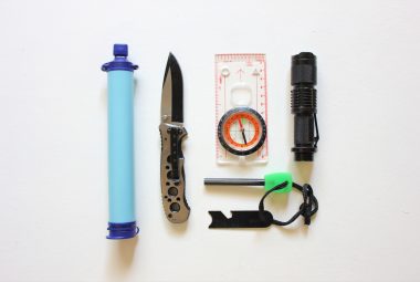 A basic emergency preparedness kit laid out flat, including a water filter, knife, compass, and flashlight
