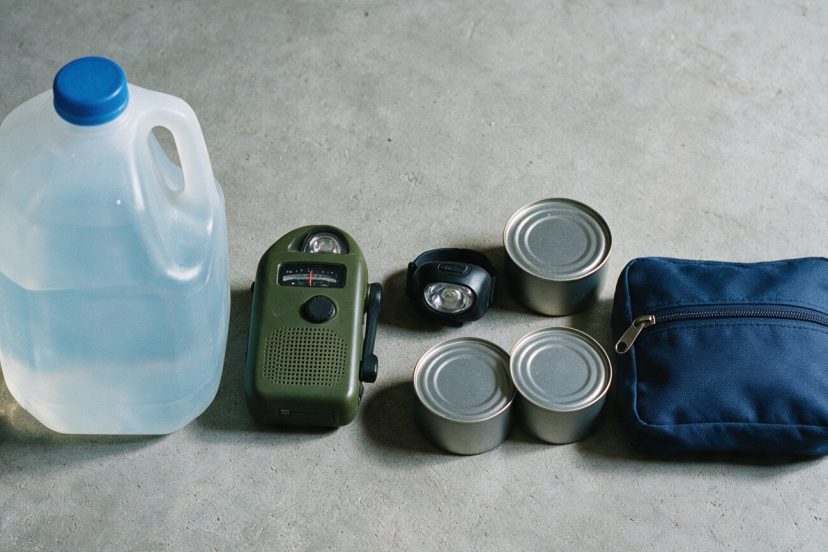 72 hour emergency checklist supplies laid out on concrete: one-gallon water jug, hand-crank emergency radio, headlamp, canned food and a first aid pouch